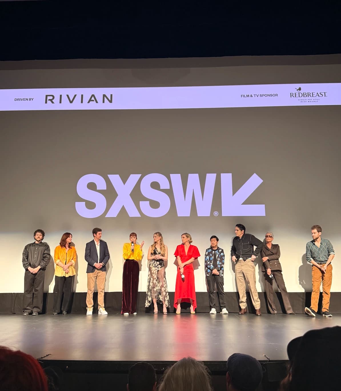 A group photo of the "Sender" film cast in front of a big SXSW screen