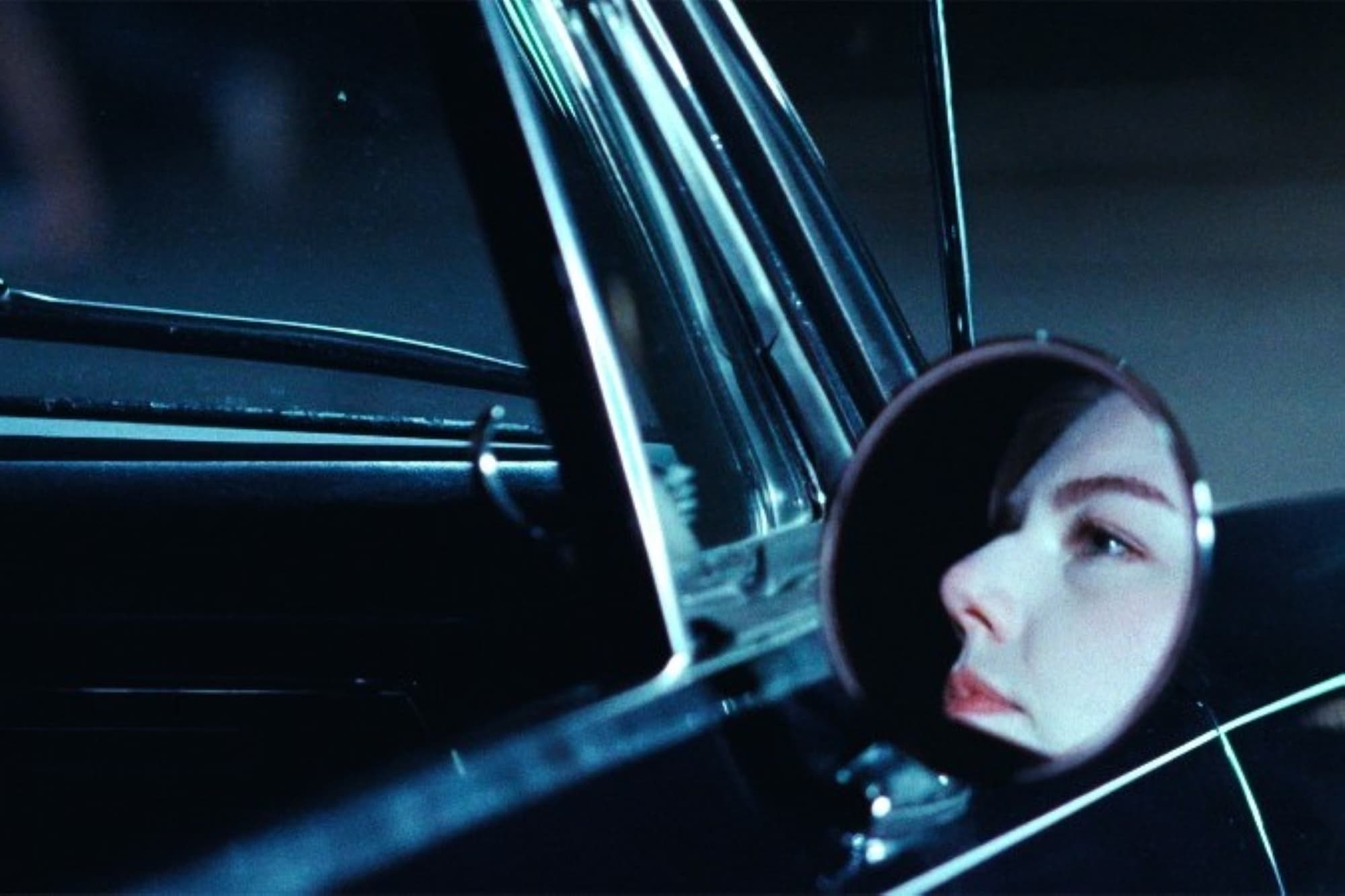 A promo photo from ‘1969: Killers, Freaks, and Radicals’ of a woman's face in a vintage car's circular external mirror