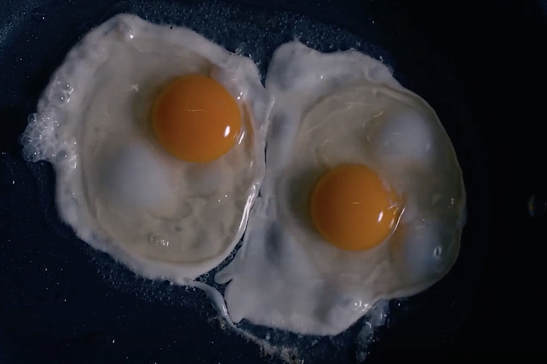Two egg yolks sizzling in a black pan, a screencapture from 'The Substance'